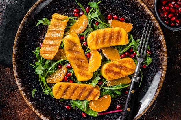 Salade d'été avec fromage Halloumi grillé oranges roquette et grenade Fond sombre Vue de dessus