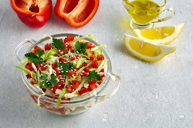 Salade d'été légère de chou blanc frais, de paprika et de persil assaisonné d'huile et de citron dans un bol de verre sur une table en pierre légère