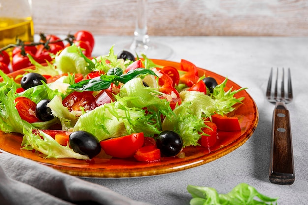 Salade d'été simple de tomates laitues aux olives et à l'huile d'olive sur une assiette rouge