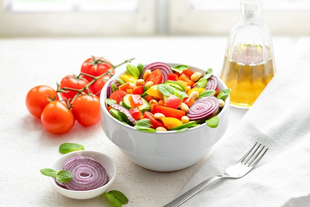 Salade d'été avec tomates cerises, concombre, poivron, oignon, basilic et cacahuètes sur le rebord de la fenêtre.