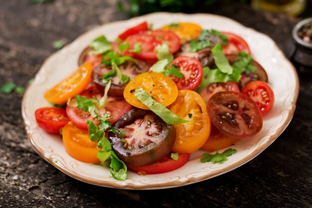 Salade d&#39;été de tomates de différentes couleurs avec des herbes vertes et du poivre.