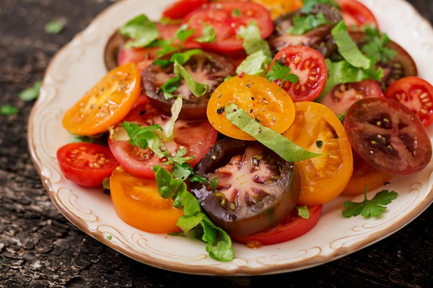 Salade d'été de tomates de différentes couleurs avec des herbes vertes et du poivre.