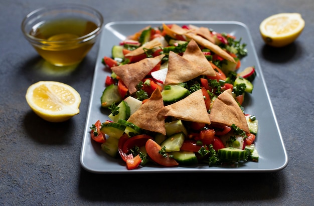 Salade Fattoush traditionnelle avec légumes et pain pita. Cuisine levantine, arabe, moyen-orientale. Servi dans une assiette rectangulaire avec du citron et de l'huile d'olive. Fond sombre. Fermer. Espace pour le texte