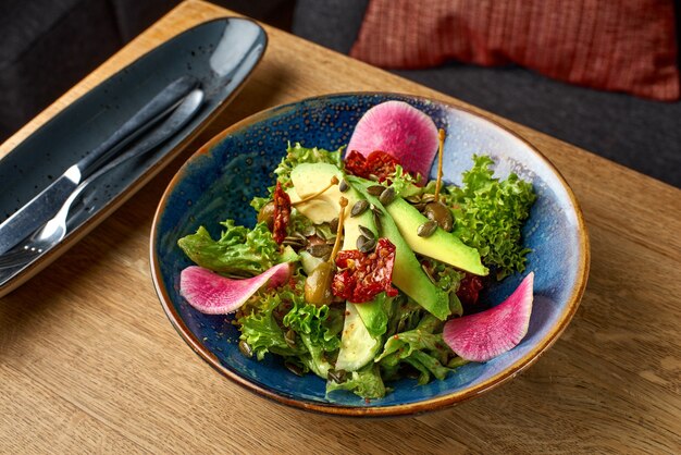 Salade fermière, avocat et radis mélanger avec de la laitue sur une table en bois