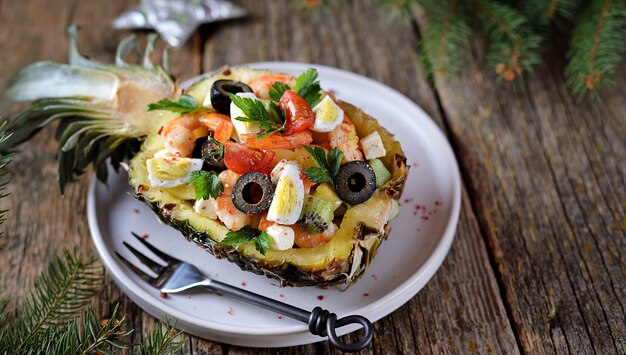 Salade festive de crevettes, kiwi, olives, fromage à pâte molle, œufs de caille, tomate cerise dans des assiettes d'ananas.