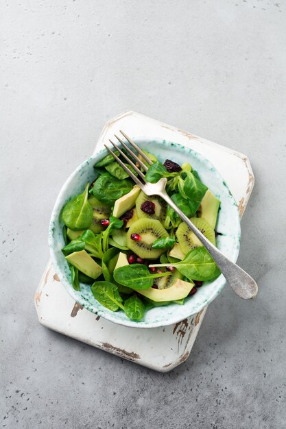 Salade de feuilles de bébé épinards, cresson, kiwi, avocat et grenade dans une vieille plaque en céramique sur un fond de béton gris