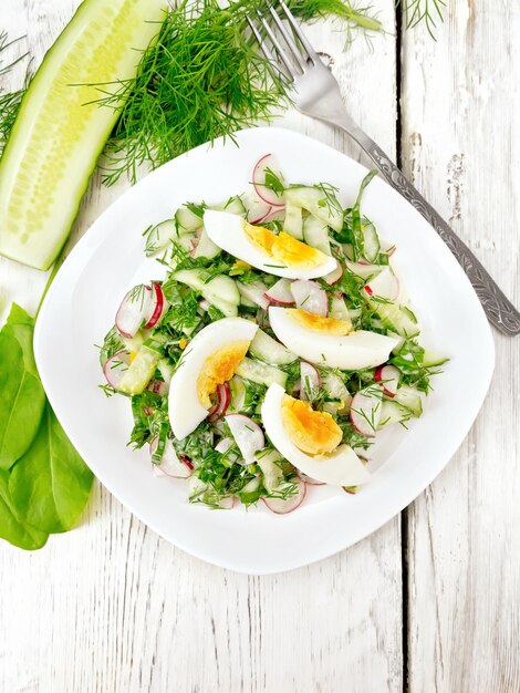 Salade de feuilles d'oseille de concombre de radis et d'œufs habillés de mayonnaise et de crème sure dans une assiette sur fond de planches de bois d'en haut