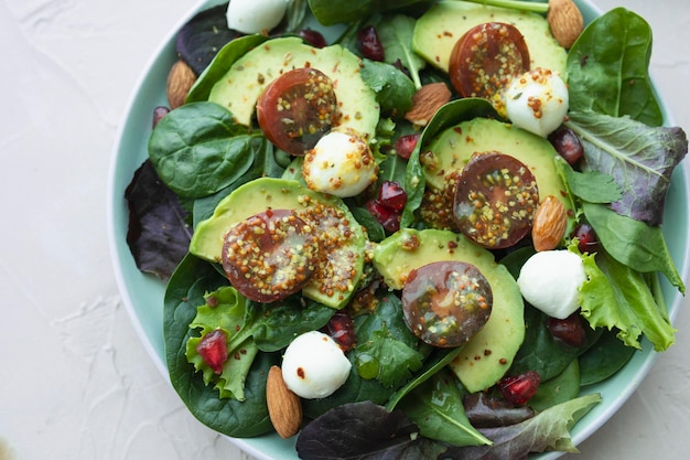 Salade de feuilles vertes avec des boules de mozzarella à la grenade et à l'avocat, tomates cerises et amandes