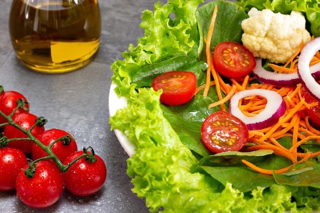Salade de feuilles vertes avec chou-fleur carotte tomate oignon avec verre d'huile d'olive en arrière-plan