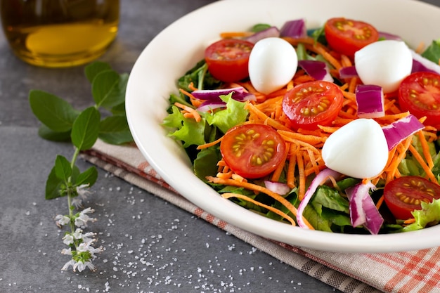 Salade de feuilles vertes près des feuilles de basilic sur une table grise avec de l'huile d'olive en arrière-plan