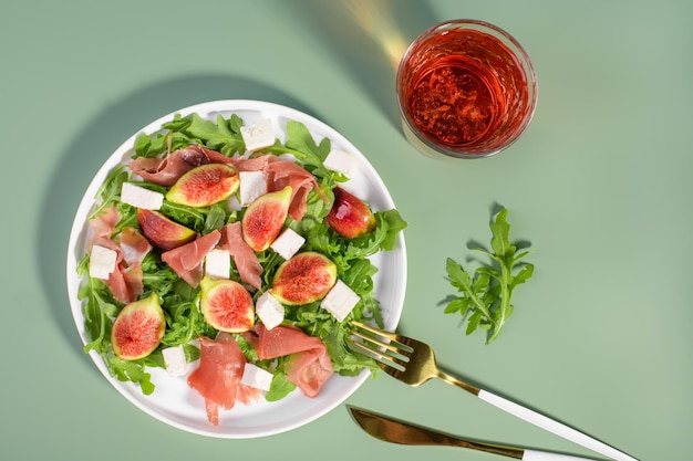 Salade de figues d'automne avec jambon cru feta de roquette dans une assiette blanche sur fond vert clair servi avec