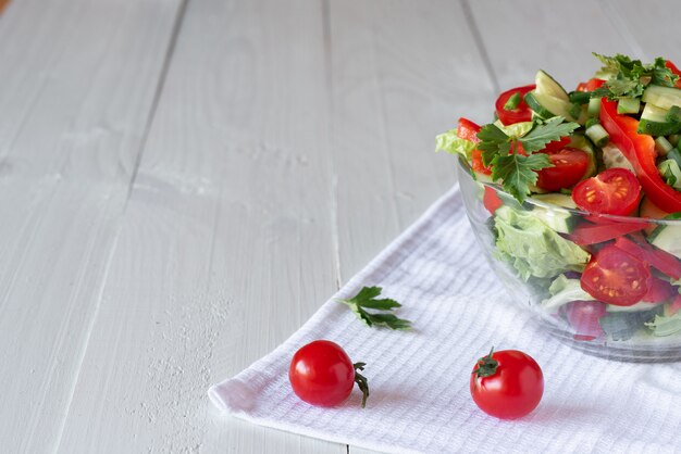 Salade sur un fond en bois blanc de tomates, concombre, laitue et poivron rouge. Concept d'alimentation saine.