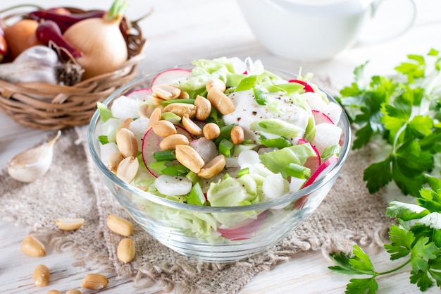 Salade fraîche au chou, radis et cacahuètes. Bol à déjeuner végétalien sain sur une table en bois blanche.