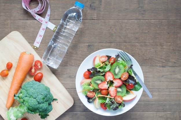 Salade fraîche aux fraises, au kiwi, aux tomates et aux pommes avec une bouteille d&#39;eau, un régime et un concept de fitness