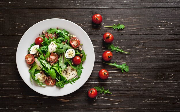 Salade fraîche aux tomates, légumes verts mélangés, noix, œufs, sur fond de bois. Nourriture saine.