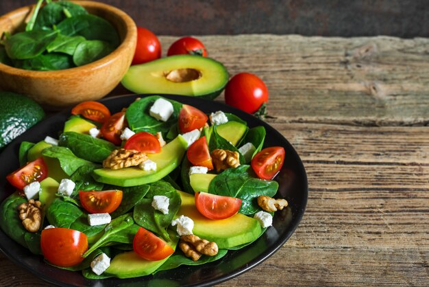 Salade fraîche d'avocat, d'épinards, de tomates cerises, de fromage feta et de noix dans une assiette sur une table en bois rustique.