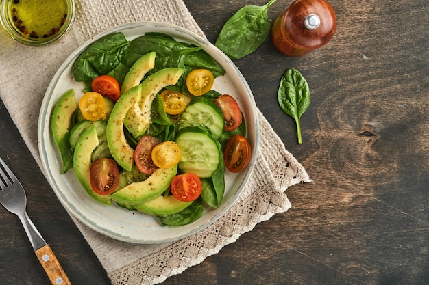 Salade fraîche d'avocat, de tomates cerises rouges, jaunes, noires, d'épinards et de concombres aux épices, au poivre et à l'huile d'olive dans un bol gris sur fond de table en bois ancien. Concept d'aliments sains. Vue de dessus.