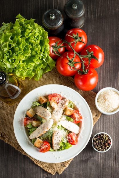 Salade fraîche à base de tomate, ruccola, poitrine de poulet, œufs, roquette, craquelins et épices. Salade César dans un bol blanc et transparent sur fond en bois