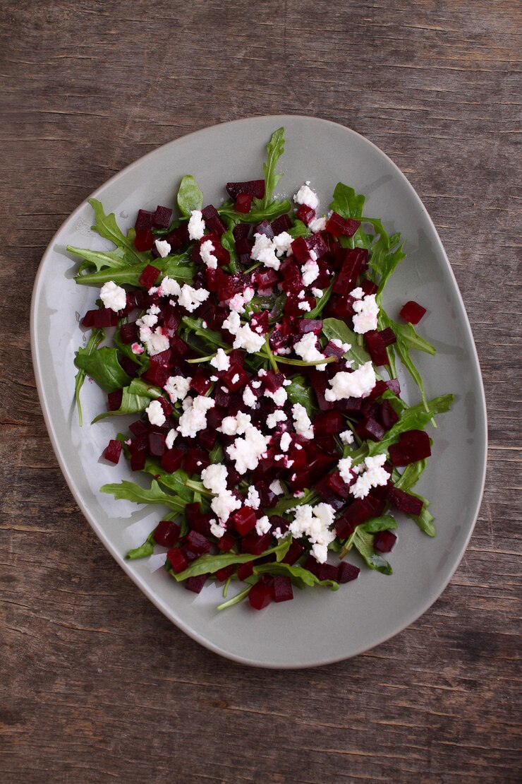 Salade fraîche à la betterave, à la roquette et à la feta dans une assiette sur fond sombre, vue de dessus.