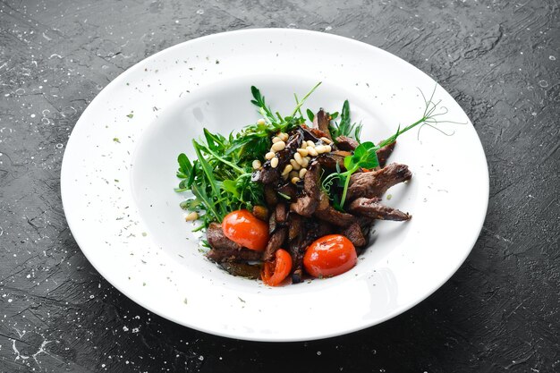 Salade fraîche avec du veau, de l'arugula, du veau, des noix de pin et des aubergines, nourriture saine sur une assiette blanche, style rustique.