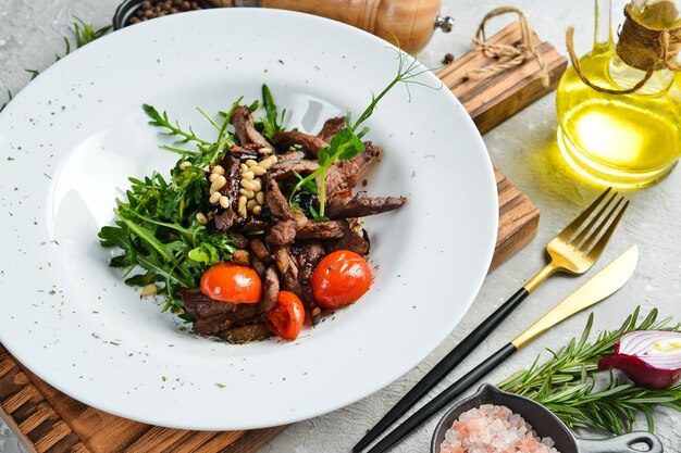 Salade fraîche avec du veau, de la roquette, des noix de pin et des aubergines, nourriture saine sur une assiette blanche, style rustique.