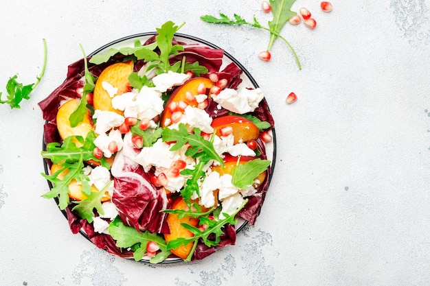 Salade fraîche avec roquette, radicchio, pêches douces, fromage feta et graines de grenade, fond de table blanche, vue de dessus