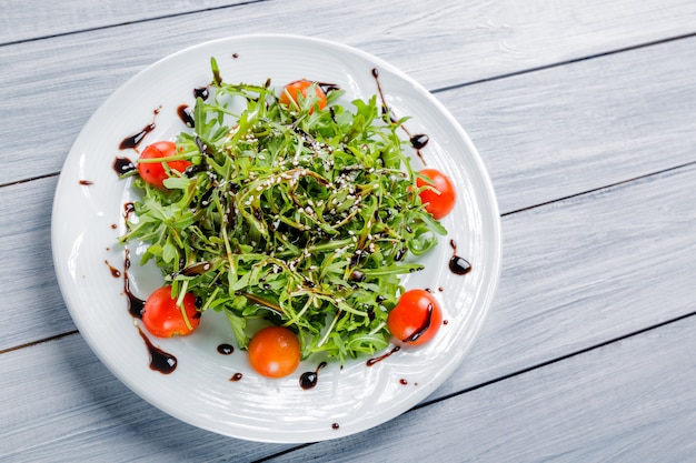 Salade fraîche de tomates cerises, laitue, bœuf et sauce sur une assiette blanche et une table en bois blanche