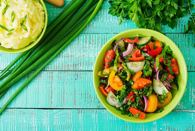 Salade fraîche de tomates, concombres, poivrons, roquette, oignon rouge et bol de purée de pommes de terre. Vue de dessus