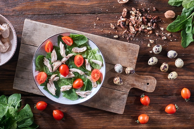 Salade fraîchement préparée en bonne santé d'oeufs de caille, de viande, de tomates et d'épinards dans une assiette sur une planche de bois sur la table de la cuisine. Déjeuner diététique. Mise à plat