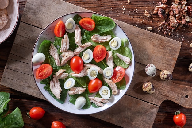 Salade fraîchement préparée saine d'œufs de caille, viande, tomates et épinards dans une assiette sur une planche de bois sur la table de la cuisine. Déjeuner diététique. Mise à plat