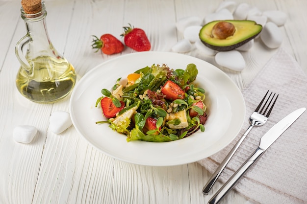 Salade de fraises au fromage brie, tomates et légumes verts Sur une assiette blanche et une table blanche