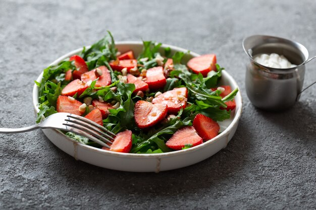 Salade de fraises à la roquette sur une assiette avec une fourchette sur fond gris clair