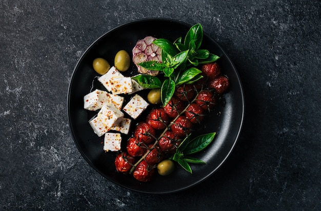 Salade avec fromage feta et cerises au four, basilic et olives sur fond noir, mise au point sélective, vue de dessus