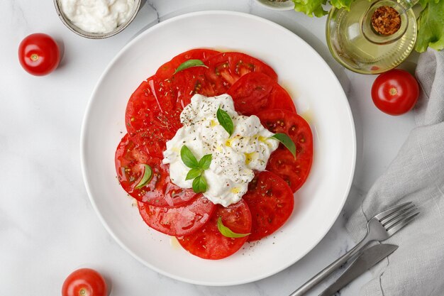 Salade de fromage stracciatella à l'huile de tomates et basilic sur plaque blanche sur fond de marbre