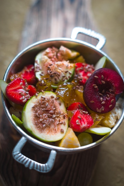 Photo salade de fruits brillante avec des figues et des fraises dans un bol en fer blanc sur un support en bois vertical