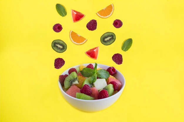 Photo salade de fruits dans le bol blanc fruits et baies sur le fond jaune copier l'espace