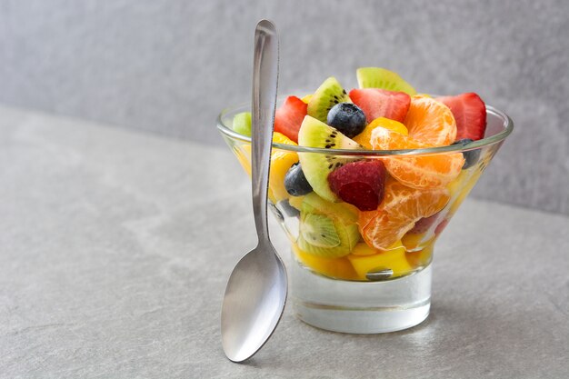 Salade de fruits dans un bol en cristal sur fond gris avec espace copie