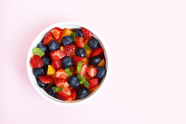 Salade de fruits dans une tasse blanche sur fond rose tendre