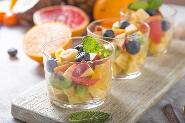 Salade de fruits dans des verres, aliments frais d'été, sains bio orange kiwi myrtilles ananas noix de coco