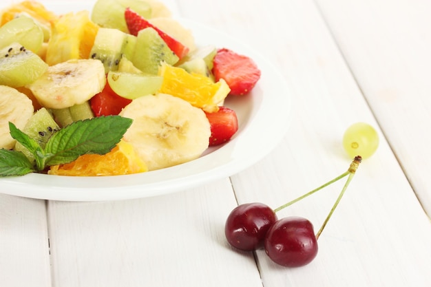 Salade de fruits frais sur assiette et baies sur table en bois blanc