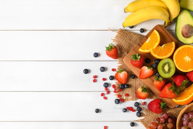 Salade de fruits frais mélangés avec des fraises, des bleuets, des oranges sur un fond blanc en bois, des fruits diététiques