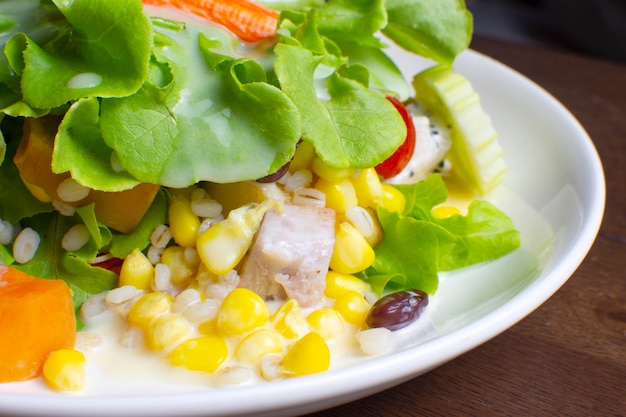 Salade de fruits et légumes frais garnie de vinaigrette dans un plat blanc sur table en bois