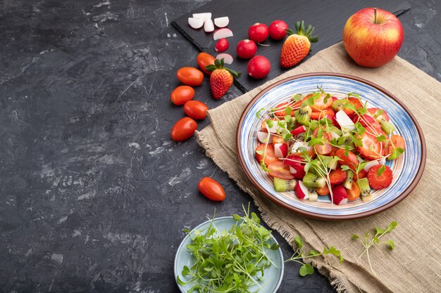 Photo salade de fruits et légumes végétariens de fraise, kiwi, tomates, germes micro-verts sur fond de béton noir.