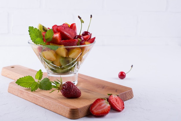 Salade de fruits mélange savoureux frais dans le bol en verre sur fond de tableau blanc. Petit-déjeuner sain aux vitamines