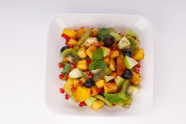 Salade de fruits mélangés disposée dans une vaisselle blanche et garnie de feuille de menthe.