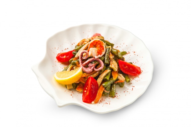 Salade de fruits de mer et légumes grillés décorée de crevettes, poulpe et citron sur fond blanc. haricots verts frits, poivrons, carottes et tomates sur un isolé