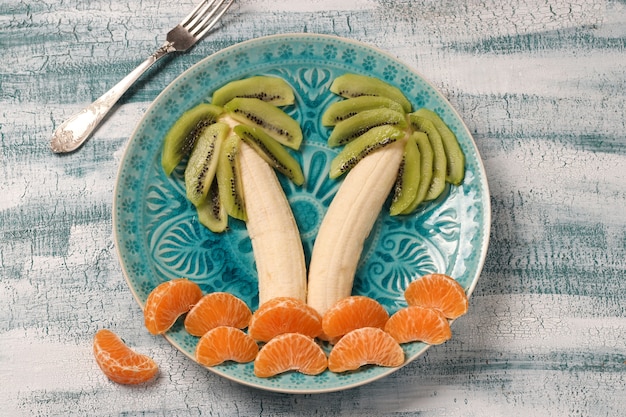 Salade de fruits sains pour les enfants de kiwi, bananes et mandarines en forme de palmier, vue de dessus