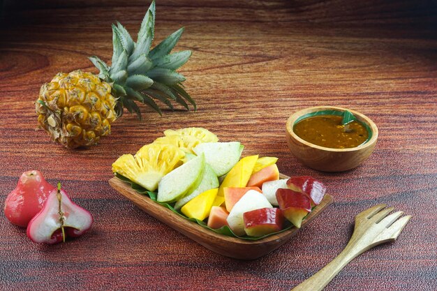 Photo salade de fruits en tranches en indonésie connue sous le nom de rujak buah ou lutis ou lotis servie avec une sauce épicée au sucre brun et des cacahuètes moulues dans une assiette sur fond de bois