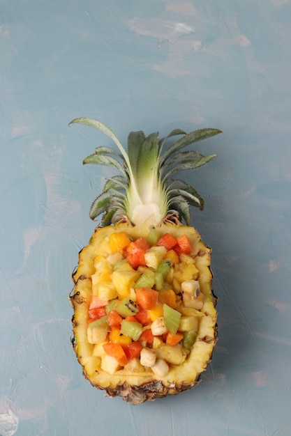 Salade de fruits tropicaux en moitiés d'ananas sur fond bleu clair, gros plan, vue de dessus, orientation verticale