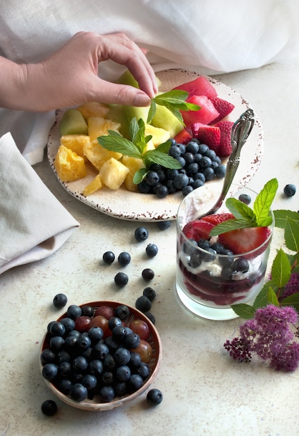 Salade de fruits et yaourt grec naturel aux baies fraîches. Main tenant des feuilles de menthe.